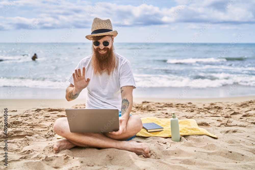 Young redhead man having video call using laptop at the beach.
