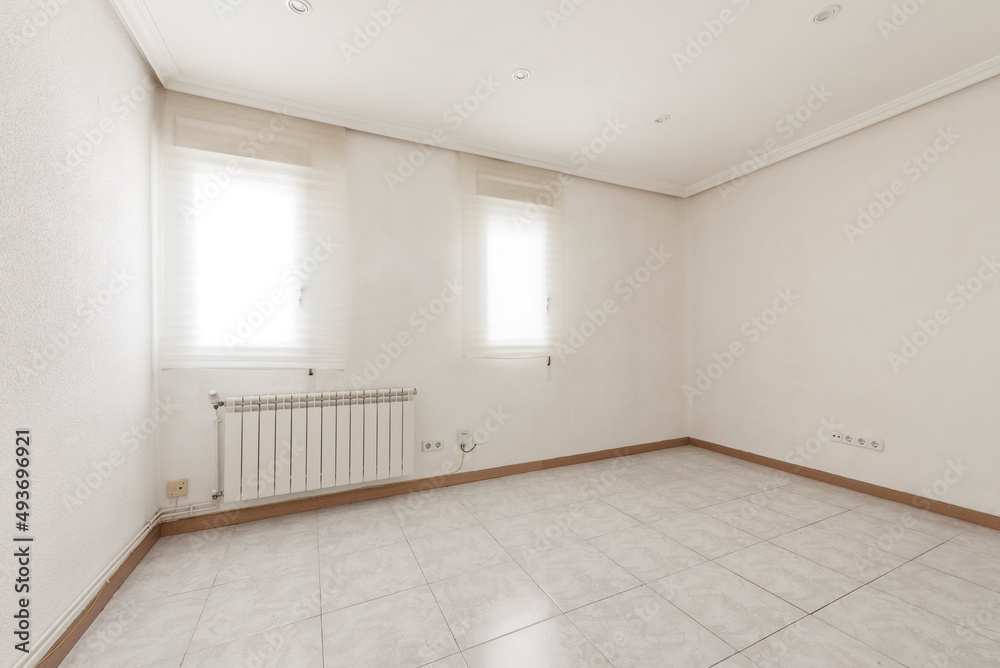 Empty room with light stoneware floor, oak baseboards, aluminum radiators, windows with translucent blinds and plaster molding on the ceiling Empty room with light stoneware floor, oak baseboards, aluminum radiators, windows with translucent blinds and plaster molding on the ceiling