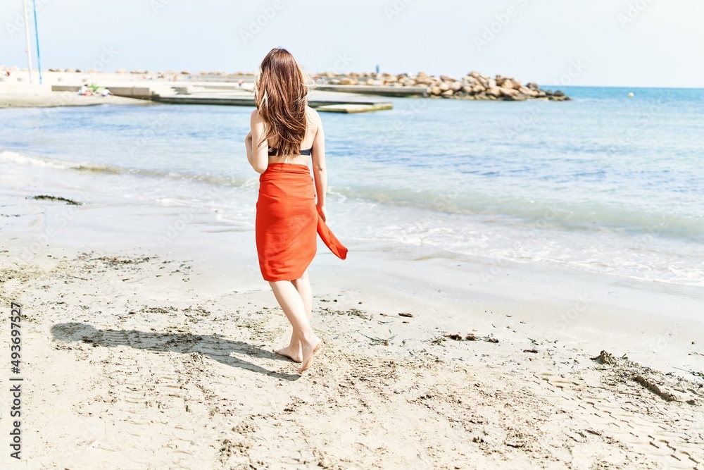 Young cuacasian girl on back view wearing bikini walking at the beach.