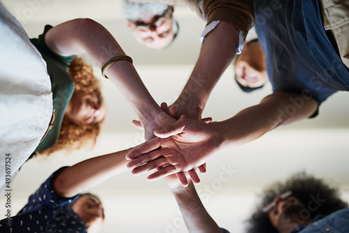 Lets get this project started. Low angle shot of a group of cheerful creative businesspeople forming a huddle with their hands inside of the office.