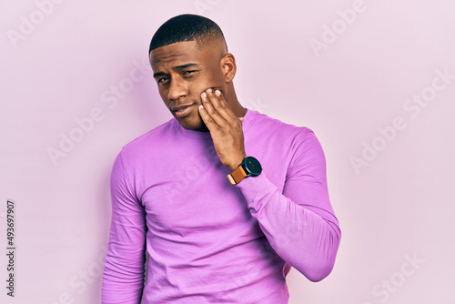 Young black man wearing casual pink sweater touching mouth with hand with painful expression because of toothache or dental illness on teeth. dentist