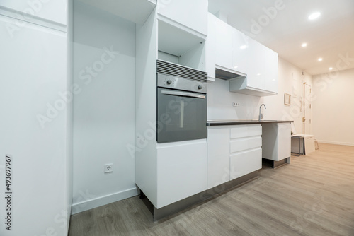 newly installed kitchen with white furniture with black countertops, gray wooden floors and convection oven