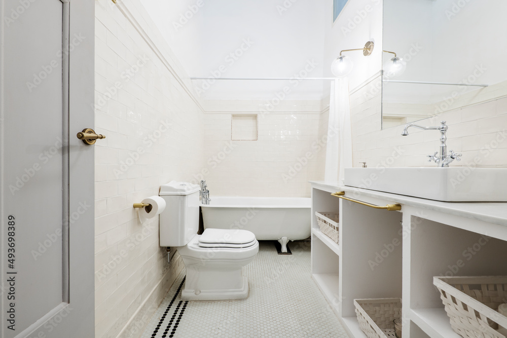 Bathroom decorated with a white porcelain sink on a white marble countertop with built-in mirrors and vintage chrome faucets and a claw-foot bathtub in the background Bathroom decorated with a white porcelain sink on a white marble countertop with built-in mirrors and vintage chrome faucets and a claw-foot bathtub in the background
