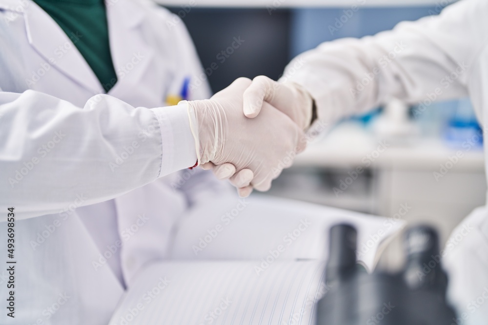 Man and woman wearing scientist uniform shake hands at laboratory Man and woman wearing scientist uniform shake hands at laboratory