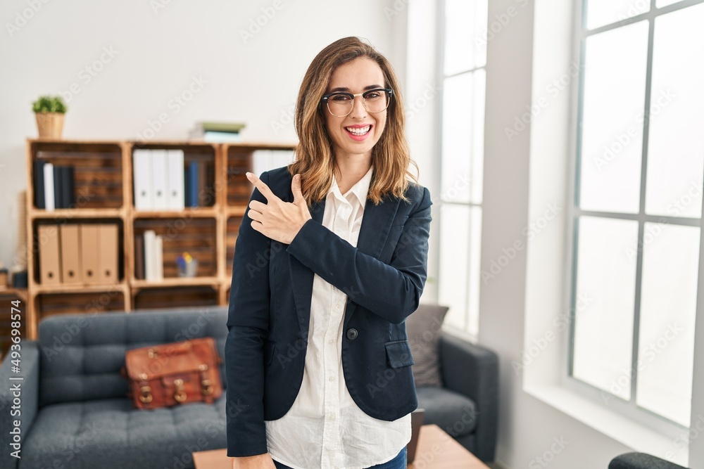 Young woman working at consultation office smiling cheerful pointing with hand and finger up to the side Young woman working at consultation office smiling cheerful pointing with hand and finger up to the side
