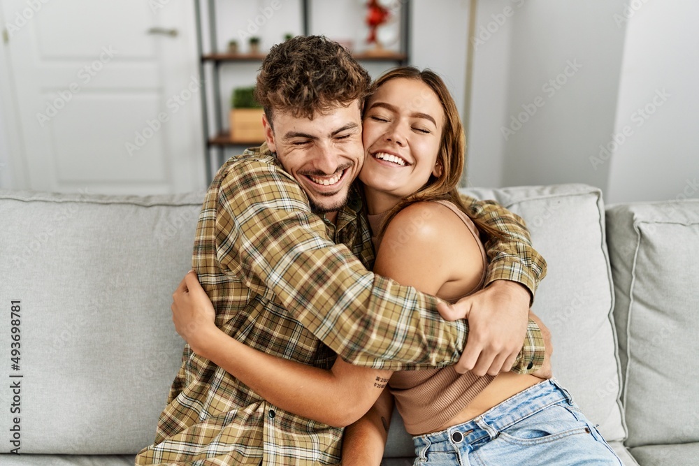 Young hispanic couple smiling happy and hugging sitting on the sofa at home. Young hispanic couple smiling happy and hugging sitting on the sofa at home.