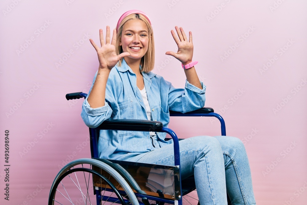 Beautiful blonde woman sitting on wheelchair showing and pointing up with fingers number ten while smiling confident and happy. Beautiful blonde woman sitting on wheelchair showing and pointing up with fingers number ten while smiling confident and happy.