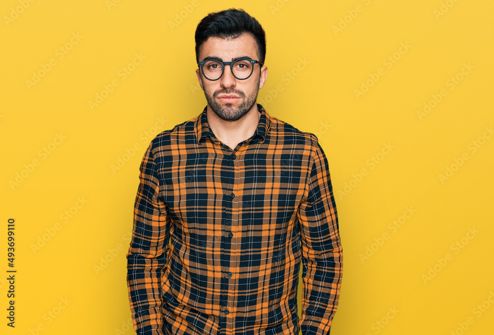 Hispanic man with beard wearing casual clothes and glasses with serious expression on face. simple and natural looking at the camera. Hispanic man with beard wearing casual clothes and glasses with serious expression on face. simple and natural looking at the camera.