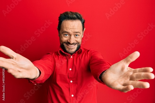 Middle age man wearing casual clothes looking at the camera smiling with open arms for hug. cheerful expression embracing happiness.