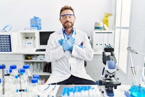 Middle age man working at scientist laboratory smiling with hands on chest with closed eyes and grateful gesture on face. health concept.