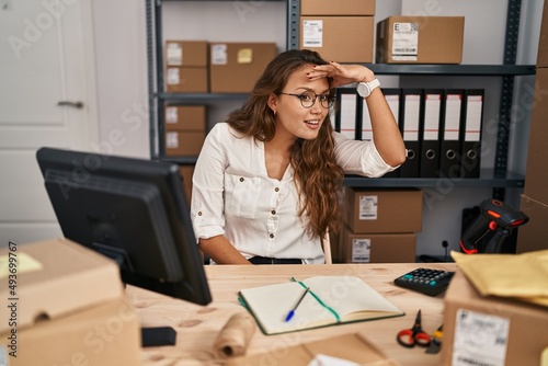 Young hispanic woman working at small business ecommerce very happy and smiling looking far away with hand over head. searching concept.