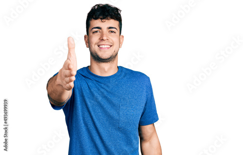 Young hispanic man wearing casual t shirt smiling friendly offering handshake as greeting and welcoming. successful business.
