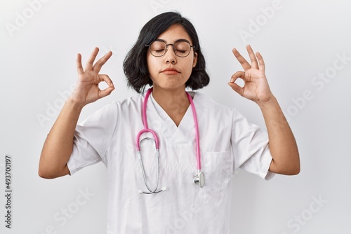 Young hispanic doctor woman wearing stethoscope over isolated background relax and smiling with eyes closed doing meditation gesture with fingers. yoga concept.