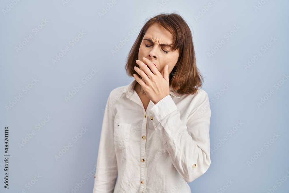Young beautiful woman standing casual over blue background bored yawning tired covering mouth with hand. restless and sleepiness. Young beautiful woman standing casual over blue background bored yawning tired covering mouth with hand. restless and sleepiness.