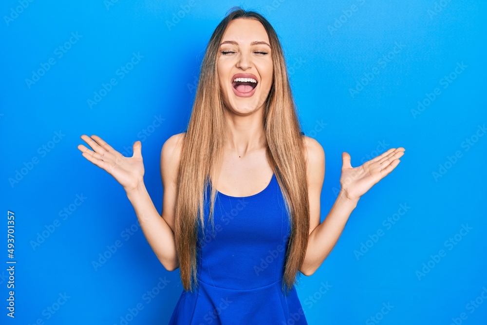 Fototapeta premium Young blonde girl wearing casual clothes celebrating mad and crazy for success with arms raised and closed eyes screaming excited. winner concept