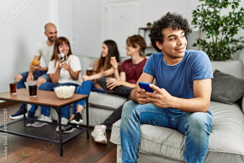 Group of young friends having party sitting on the sofa at home. Man smiling happy using smartphone at home.