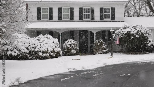 Snow falling in slow motion in front of historic home with American flag