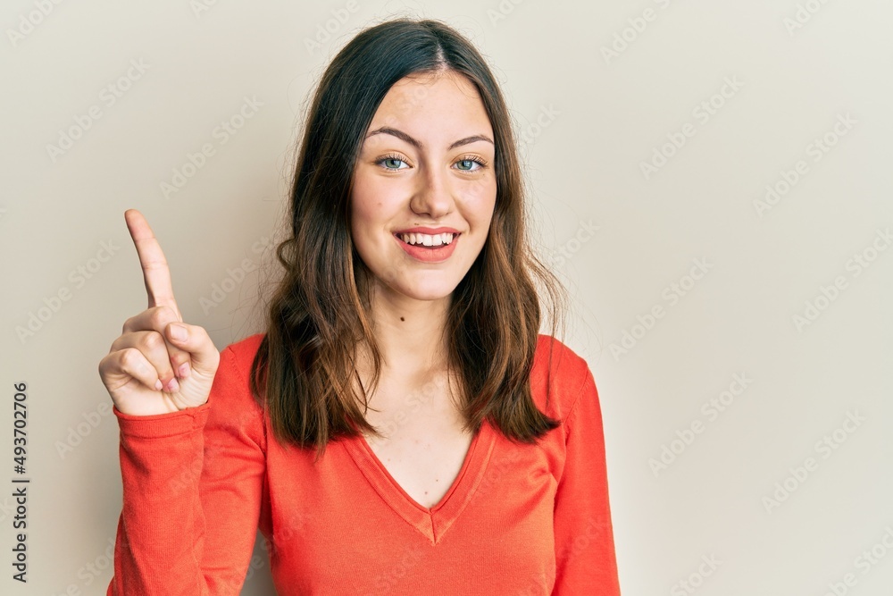 Young brunette woman wearing casual clothes showing and pointing up with finger number one while smiling confident and happy. Young brunette woman wearing casual clothes showing and pointing up with finger number one while smiling confident and happy.