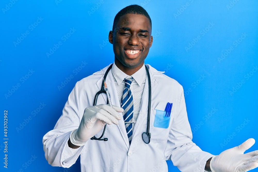 Young african american doctor man holding syringe celebrating victory with happy smile and winner expression with raised hands Young african american doctor man holding syringe celebrating victory with happy smile and winner expression with raised hands
