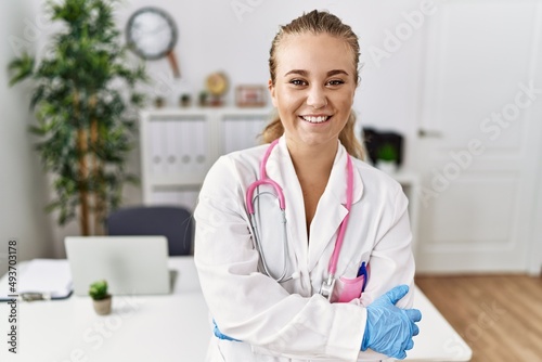 Young caucasian woman wearing doctor uniform and stethoscope at the clinic happy face smiling with crossed arms looking at the camera. positive person.