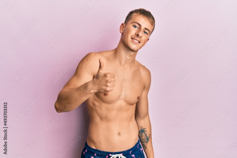 Young caucasian man wearing swimwear doing happy thumbs up gesture with hand. approving expression looking at the camera showing success.