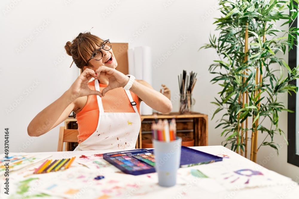 Hispanic woman at art studio smiling in love showing heart symbol and shape with hands. romantic concept. Hispanic woman at art studio smiling in love showing heart symbol and shape with hands. romantic concept.
