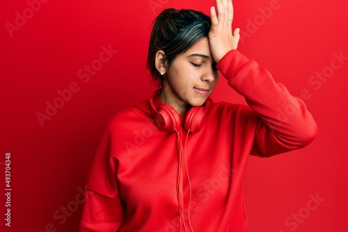 Young latin woman listening to music using headphones surprised with hand on head for mistake, remember error. forgot, bad memory concept. © Krakenimages.com