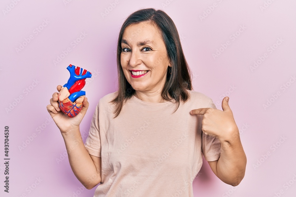 Middle age hispanic woman holding heart organ pointing finger to one self smiling happy and proud Middle age hispanic woman holding heart organ pointing finger to one self smiling happy and proud