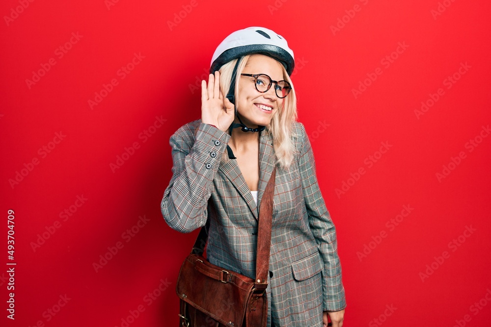 Beautiful caucasian blonde business woman wearing bike helmet smiling with hand over ear listening an hearing to rumor or gossip. deafness concept. Beautiful caucasian blonde business woman wearing bike helmet smiling with hand over ear listening an hearing to rumor or gossip. deafness concept.