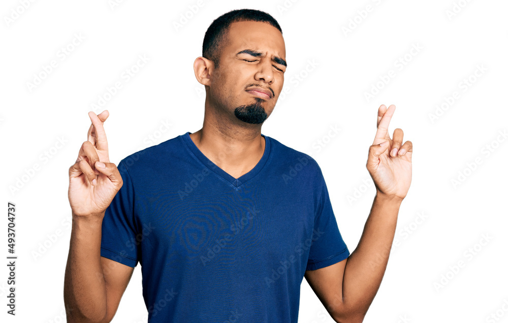 Young african american man wearing casual t shirt gesturing finger crossed smiling with hope and eyes closed. luck and superstitious concept. Young african american man wearing casual t shirt gesturing finger crossed smiling with hope and eyes closed. luck and superstitious concept.