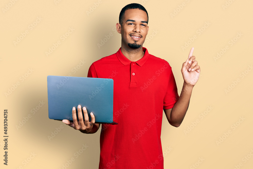 Young african american man working using computer laptop surprised with an idea or question pointing finger with happy face, number one Young african american man working using computer laptop surprised with an idea or question pointing finger with happy face, number one