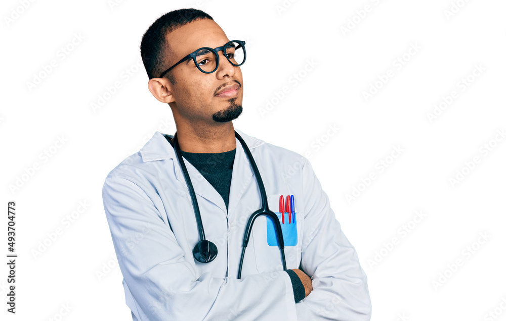 Young african american man wearing doctor uniform and stethoscope looking to the side with arms crossed convinced and confident Young african american man wearing doctor uniform and stethoscope looking to the side with arms crossed convinced and confident