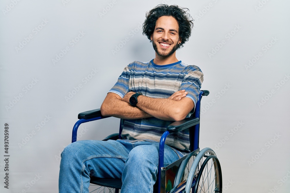Handsome hispanic man sitting on wheelchair happy face smiling with crossed arms looking at the camera. positive person. Handsome hispanic man sitting on wheelchair happy face smiling with crossed arms looking at the camera. positive person.