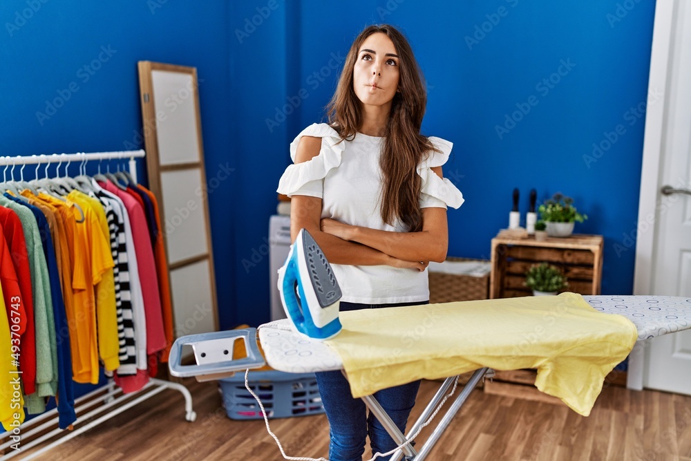 Young hispanic woman ironing clothes at laundry room making fish face with lips, crazy and comical gesture. funny expression.