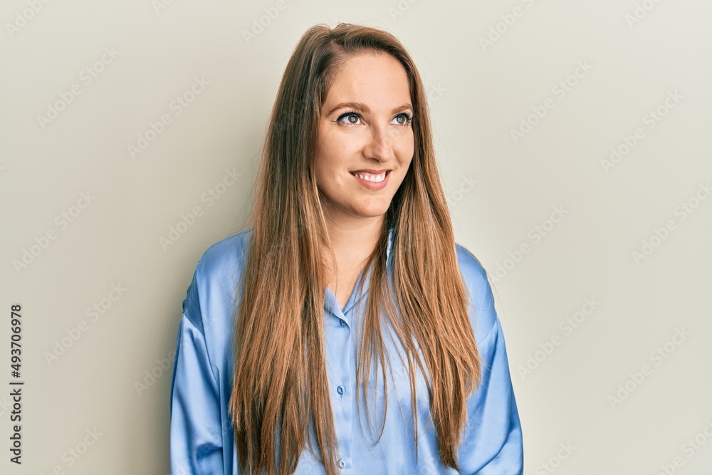 Young blonde woman wearing casual blue shirt looking away to side with smile on face, natural expression. laughing confident. Young blonde woman wearing casual blue shirt looking away to side with smile on face, natural expression. laughing confident.