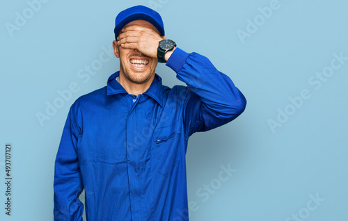 Bald man with beard wearing builder jumpsuit uniform smiling and laughing with hand on face covering eyes for surprise. blind concept.