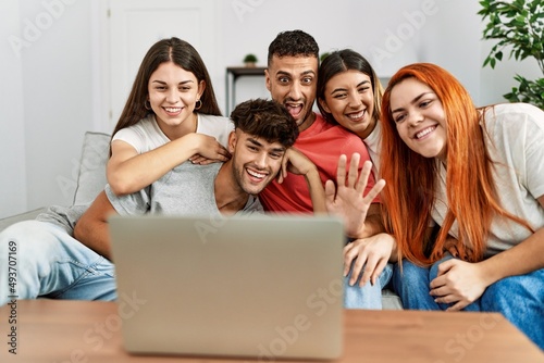 Group of young friends having video call using laptop sitting on the sofa at home.
