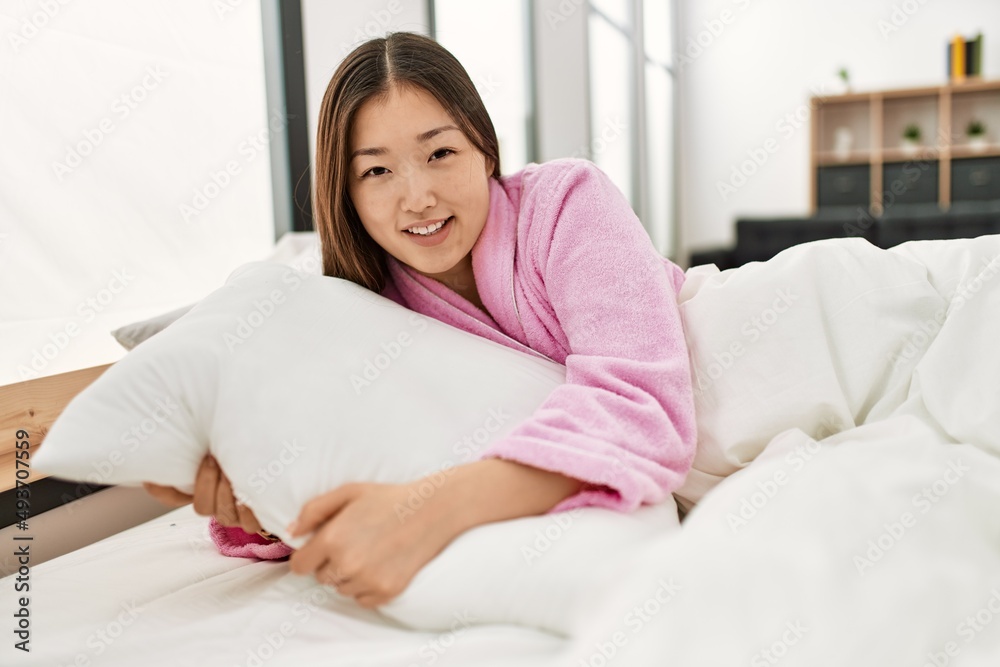 ¡Young chinese girl smiling happy and hugging pillow lying on the bed at bedroom.