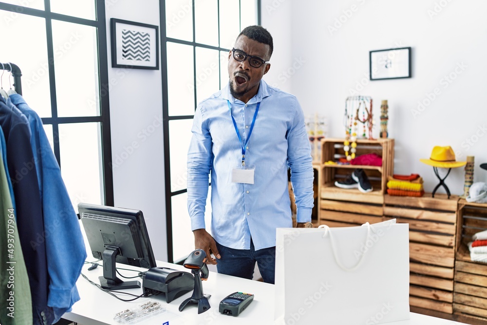 Young african man working as manager at retail boutique in shock face, looking skeptical and sarcastic, surprised with open mouth
