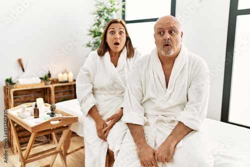 Middle age hispanic couple wearing bathrobe at wellness spa afraid and shocked with surprise expression, fear and excited face. © Krakenimages.com