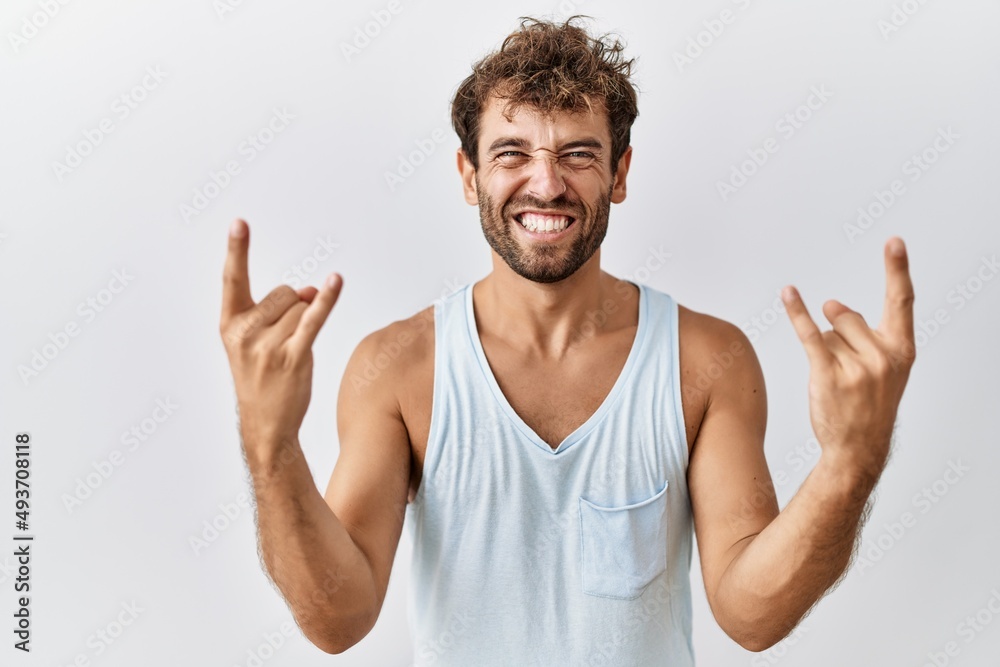 Young handsome man standing over isolated background shouting with crazy expression doing rock symbol with hands up. music star. heavy concept. Young handsome man standing over isolated background shouting with crazy expression doing rock symbol with hands up. music star. heavy concept.