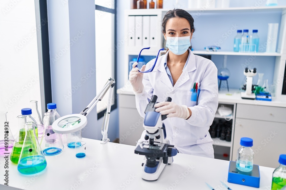 Young hispanic woman wearing scientist uniform using microscope at laboratory Young hispanic woman wearing scientist uniform using microscope at laboratory