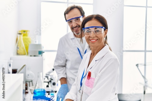 Middle age man and woman partners wearing scientist uniform looking to the camera at laboratory