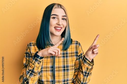 Young modern girl wearing casual yellow shirt smiling and looking at the camera pointing with two hands and fingers to the side. © Krakenimages.com