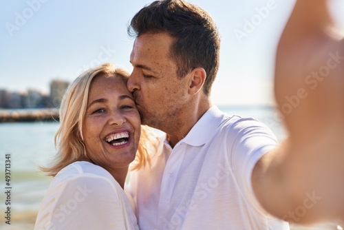 Middle age man and woman couple hugging each other and kissing make selfie by the smartphone at seaside