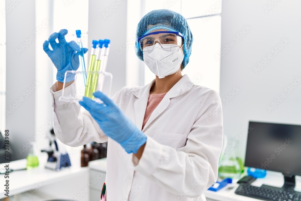 Young latin woman wearing scientist uniform holding test tube at laboratory