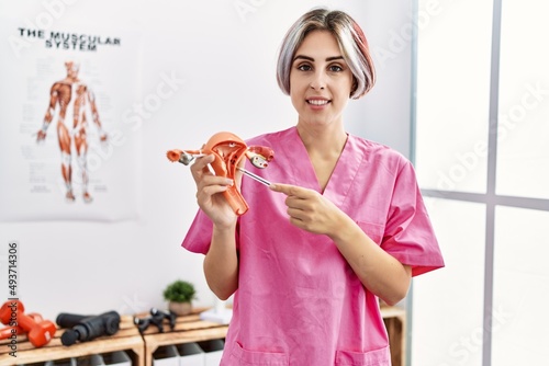Young caucasian gynecologist woman holding fallopian tube anatomical model standing at the clinic. photo