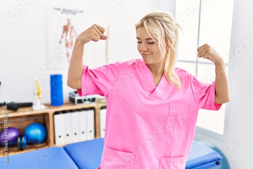 Young caucasian woman working at pain recovery clinic showing arms muscles smiling proud. fitness concept.