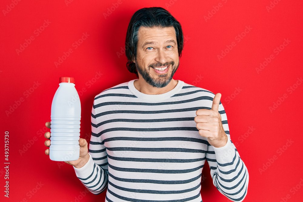Middle age caucasian man holding liter bottle of milk smiling happy and positive, thumb up doing excellent and approval sign Middle age caucasian man holding liter bottle of milk smiling happy and positive, thumb up doing excellent and approval sign