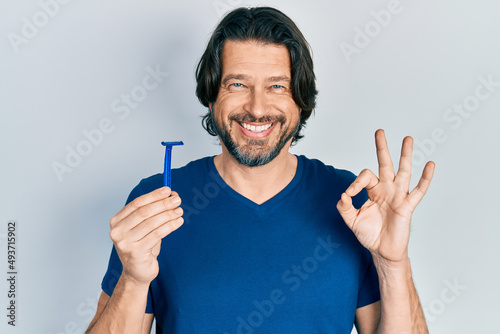 Middle age caucasian man holding razor doing ok sign with fingers, smiling friendly gesturing excellent symbol